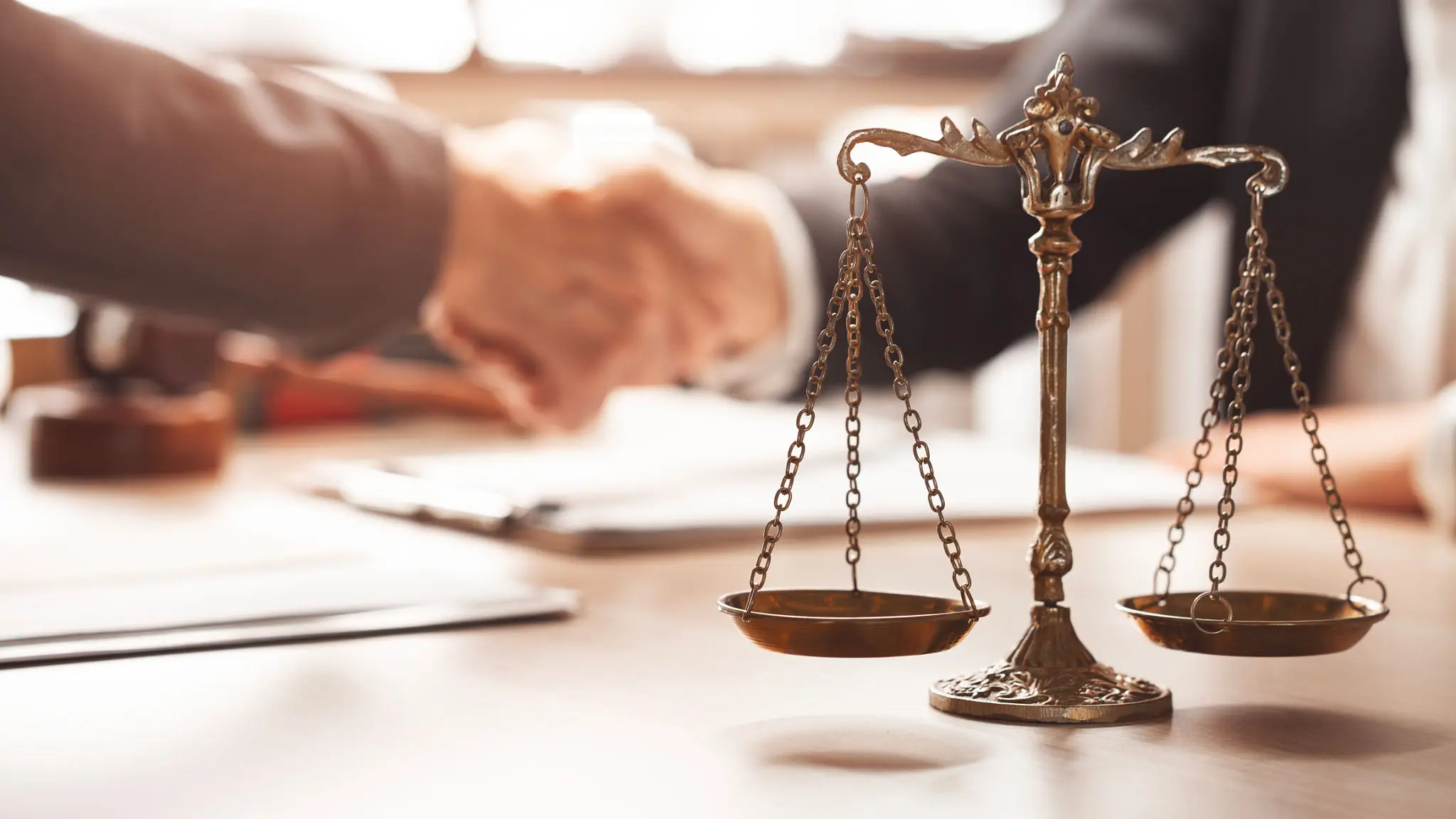 Two people shaking hands with scales of justice in foreground.